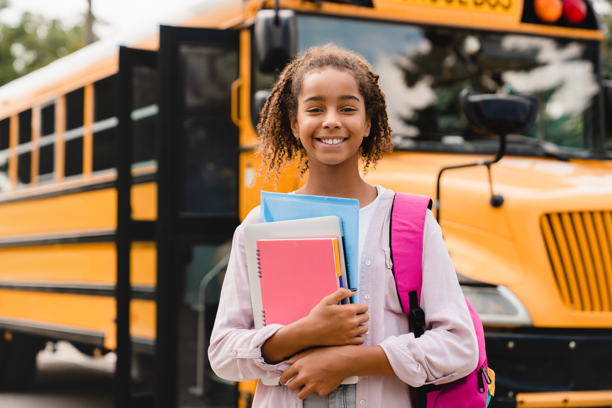 A happy student standing in front of a bus after her shorter school day.